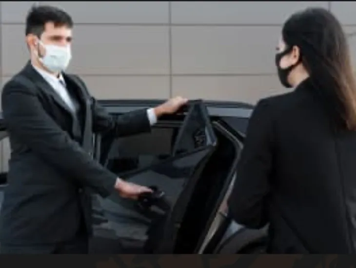 Professionele chauffeur in pak opent de deur van een zwarte premium wagen